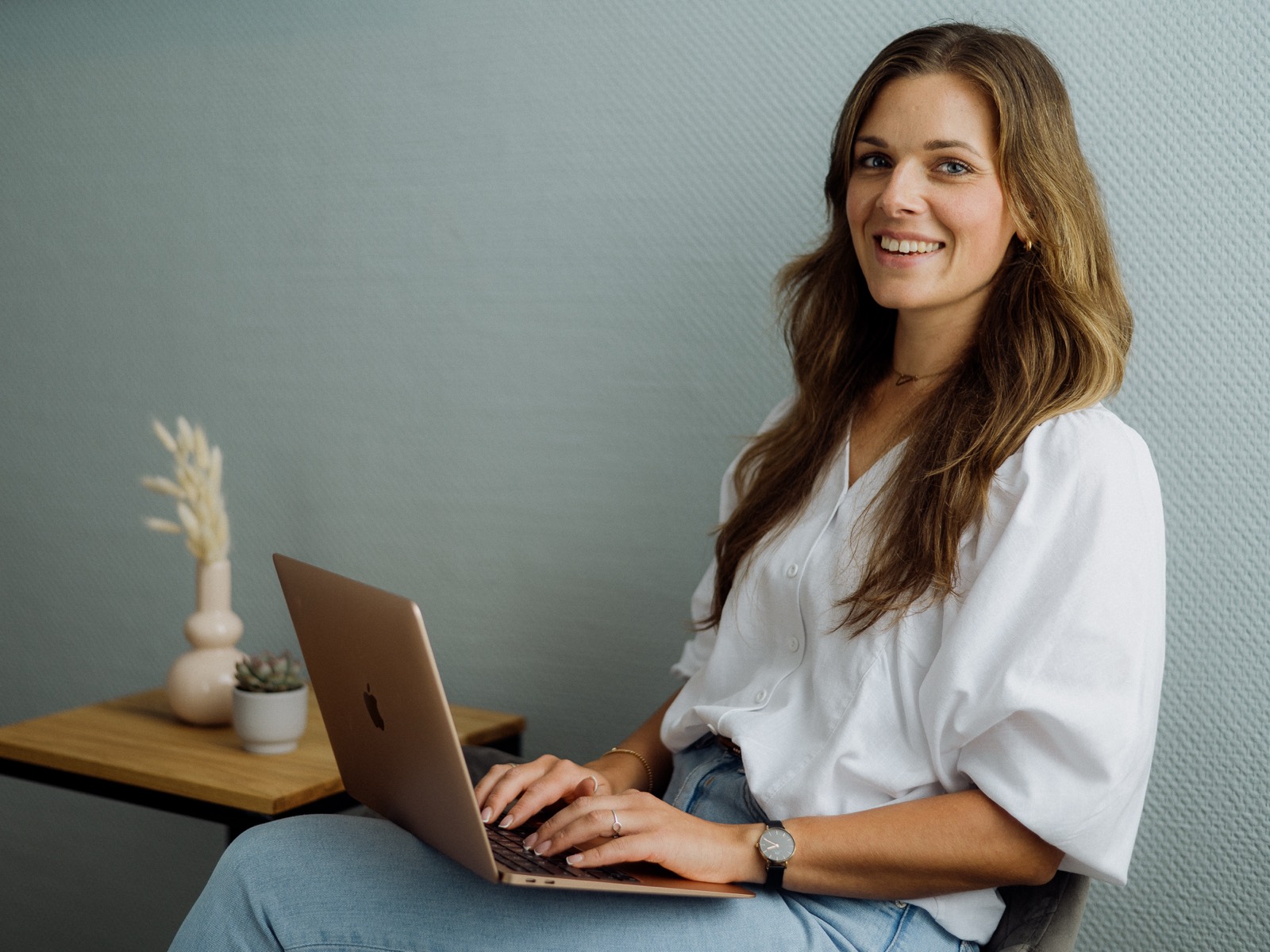 Stefanie Fronert sitzt lächelnd mit ihrem Laptop, bereit für eine Online-Sitzung