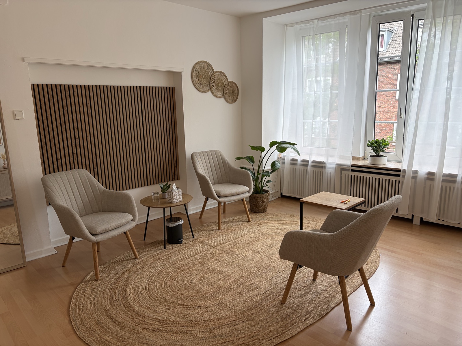 Heller Therapieraum mit drei Sesseln, Rundteppich und großen Fenstern