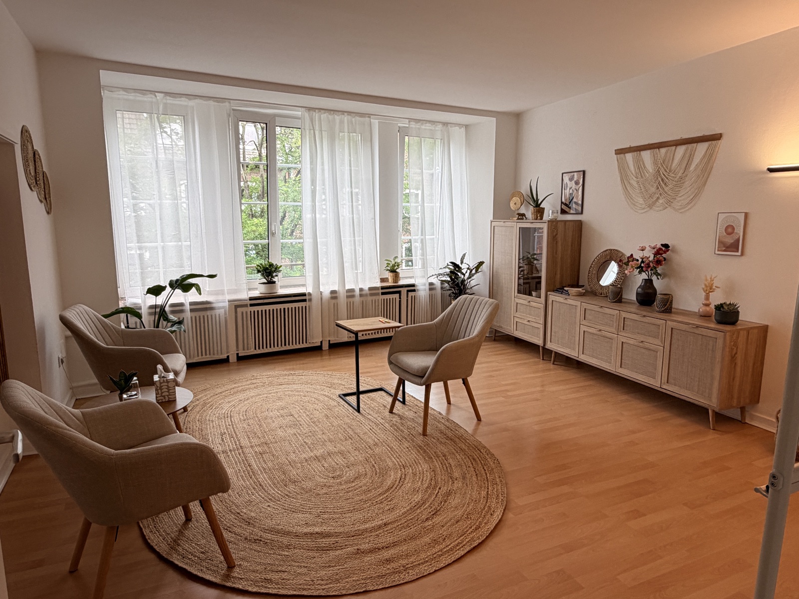 Lichtdurchfluteter Praxisraum mit Sesseln, Sideboard und Blick ins Grüne